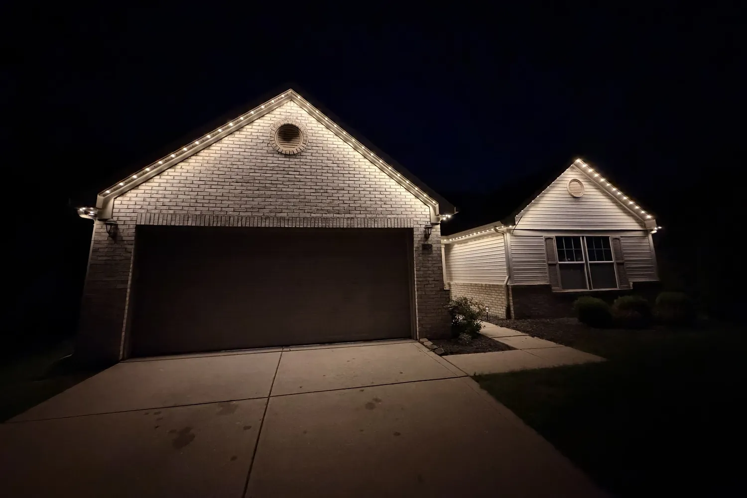 Permanent LED lighting in warm white along the rooflines of a brick home at night