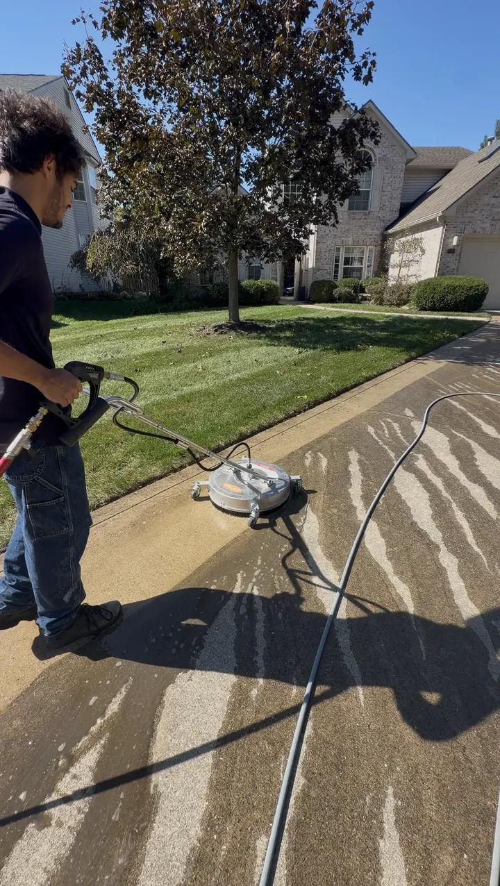 Lakeline Exteriors technician pressure washing a concrete driveway with a surface cleaner in Fishers, IN